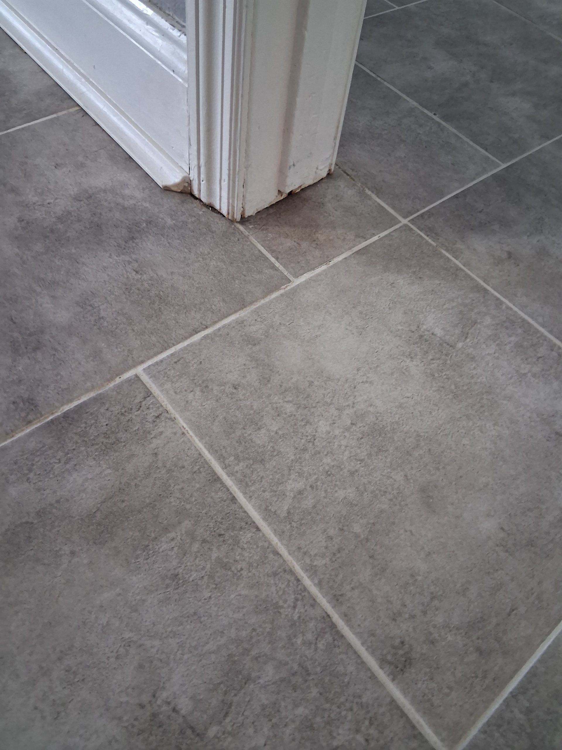 Grey stone-look tile floor with light grout lines, photographed at the base of a white door frame.