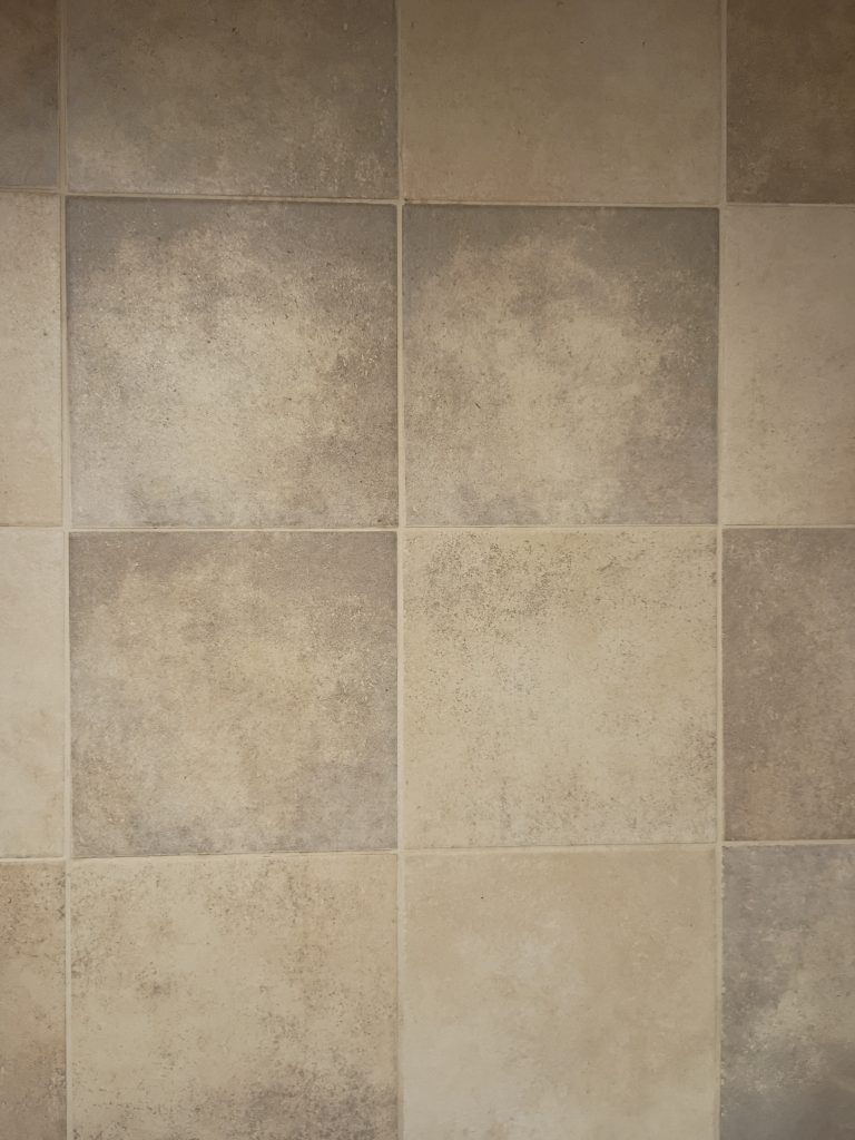 Tan tile floor laid in a diamond pattern beneath wooden kitchen cabinets.