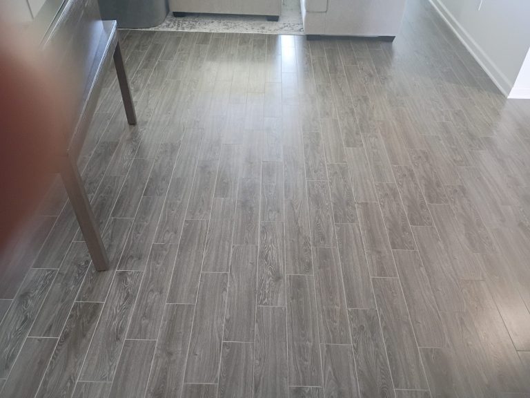 Grey wood-look plank floor tile, viewed from above near a table leg.