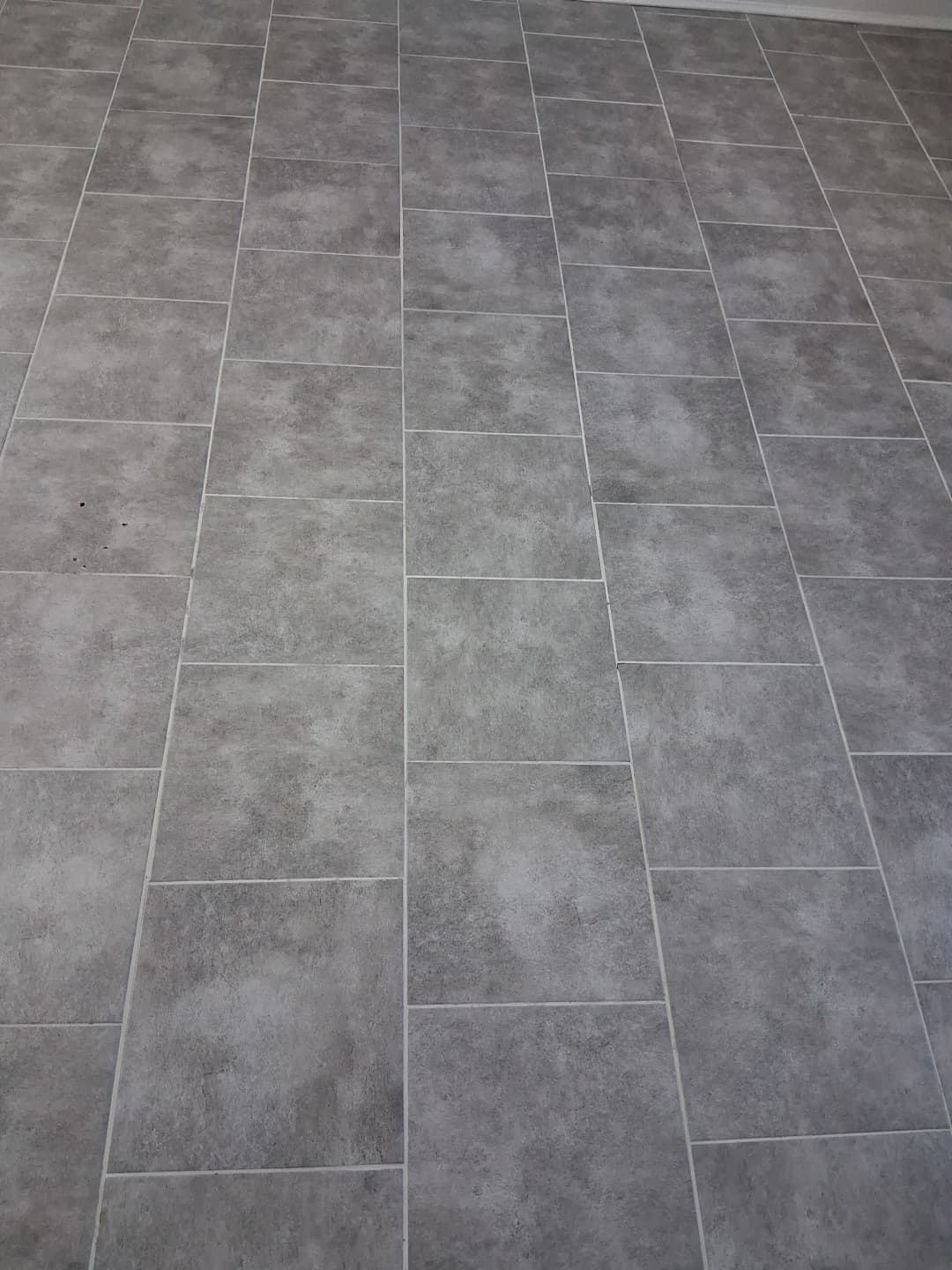Grey stone-look rectangular tile floor laid in a brick pattern with white grout, viewed from above.